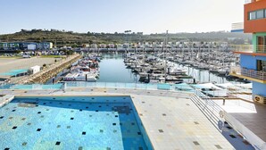 Un port de plaisance avec des bateaux amarrés, une piscine et un bâtiment à la façade bleue et orange.