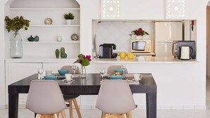Uma cozinha moderna com área de refeições, destacando uma mesa de jantar preta, duas cadeiras cinzas, um armário branco com objetos decorativos e um micro-ondas.