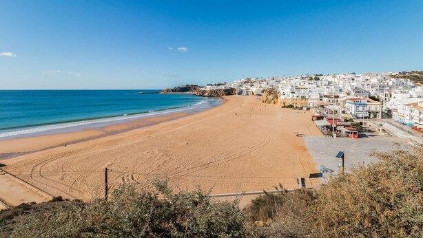 Uma cidade costeira com uma extensa praia de areia, mar azul cristalino e edifícios brancos ao longo da costa.