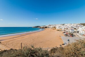 A coastal town with a wide sandy beach, a clear blue sea, and white buildings along the shore.