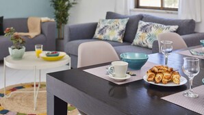 Uma área de refeições com uma mesa de madeira escura, cadeiras brancas, um prato de croissants, uma xícara branca e uma tigela azul.