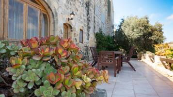 A stone building with a patio area featuring a potted plant, wooden furniture, and a stone wall.