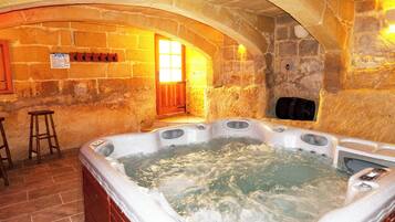 A stone-walled room with a hot tub, wooden stools, and a bench.