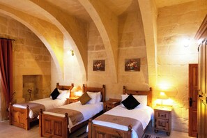 A room with two wooden beds, each with a nightstand and a lamp, in a stone-walled room with arched ceilings.