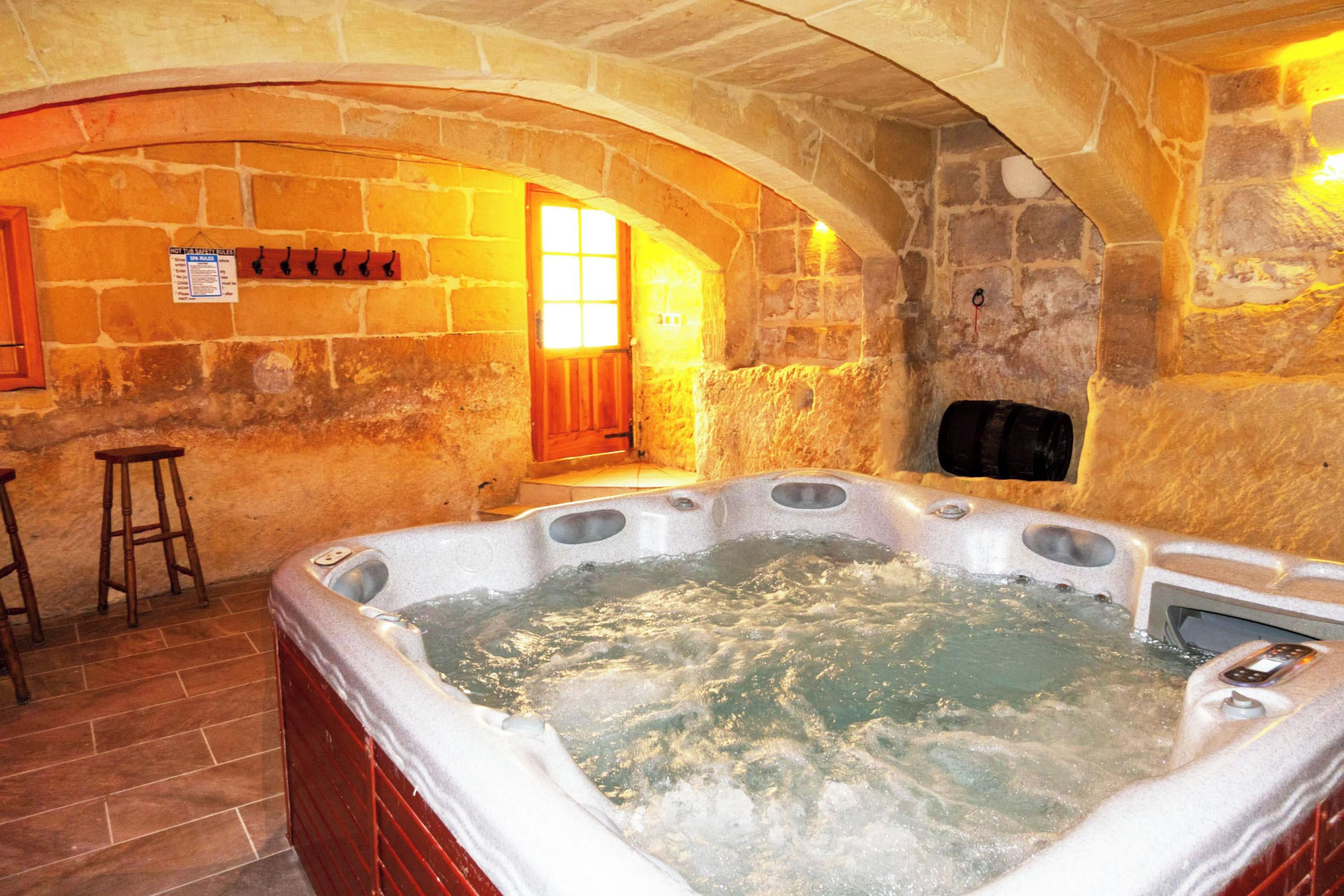 Habitació de pareds de pedra amb banyera d'hidromassatge, tamborets de fusta i una banca.