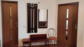 Een kamer met twee houten deuren, een bankje, een stoel, een spiegel en een vloerkleed.