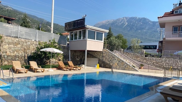 A swimming pool with lounge chairs, a lifeguard tower, and a mountain backdrop. - Bella Rose Hotel (Fethiye)