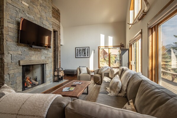 A cozy living room with a stone fireplace, leather sofa, and a large window offering a view of the outdoors.