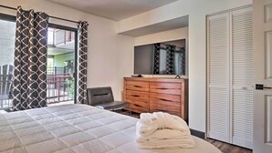 Ein Schlafzimmer mit einem Bett, einer Holzkommode, einem Sessel und einem Balkon mit gemusterten Vorhängen.