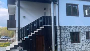 Una casa moderna de dos plantas con tejado de tejas rojas, fachada de piedra y una escalera negra que lleva a la entrada.