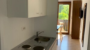 Een compacte keuken met een ingebouwde kookplaat en gootsteen, een houten eettafel en uitzicht op de omgeving via een schuifdeur.