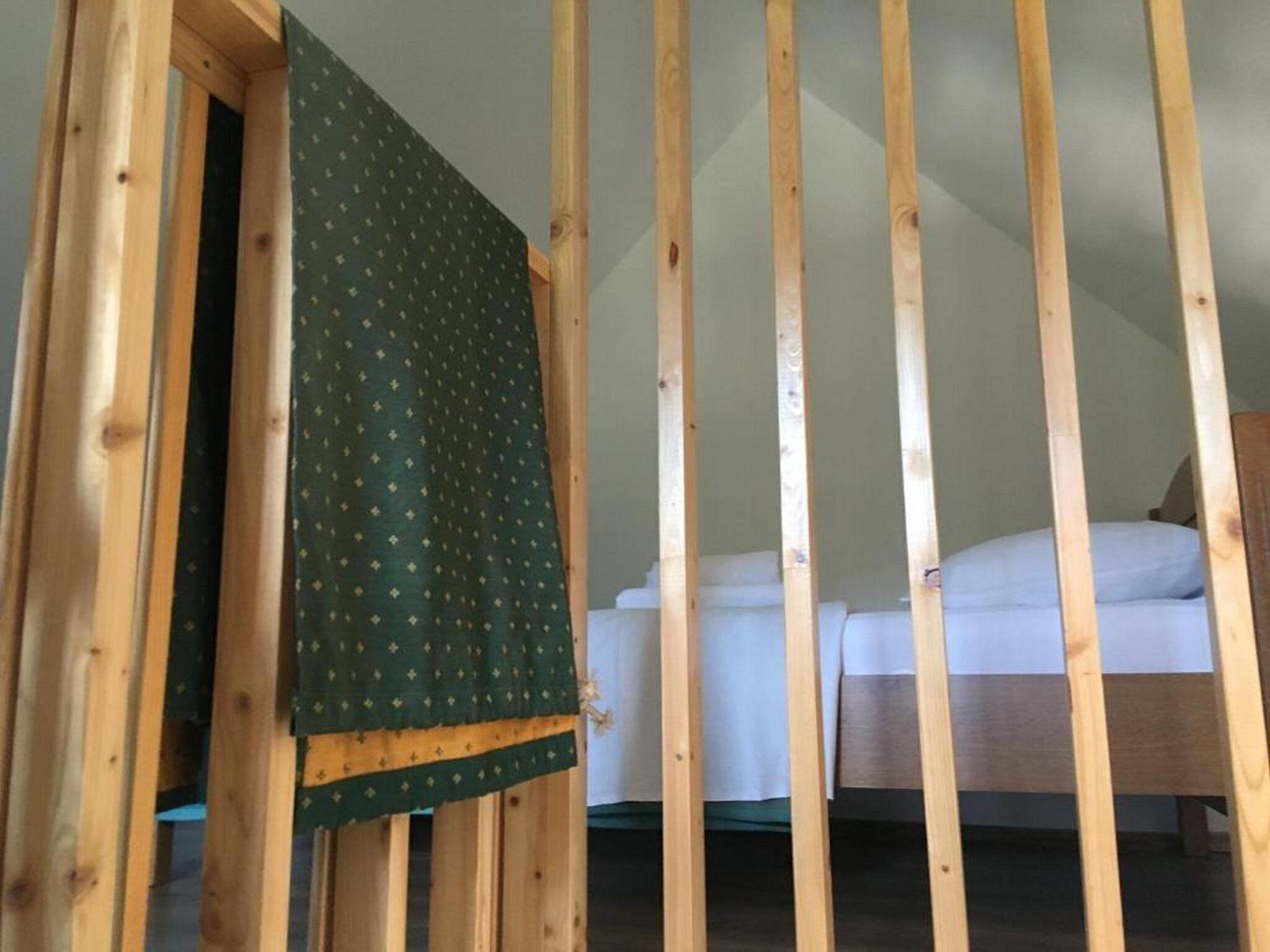 A room with a wooden slatted ceiling, a bed with white bedding, and a green patterned curtain.