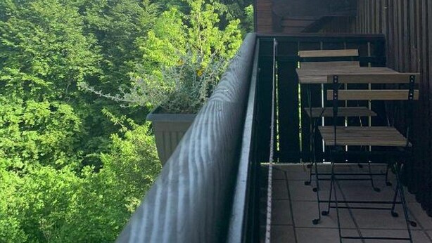Een balkon met uitzicht op weelderige groene bomen, een houten hekwerk en een metalen tafel met stoelen.
