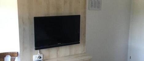 Ein Zimmer mit einem an der Wand montierten Fernseher, einem kleinen, weißen Kühlschrank und einer Wand mit Holzpaneelen.