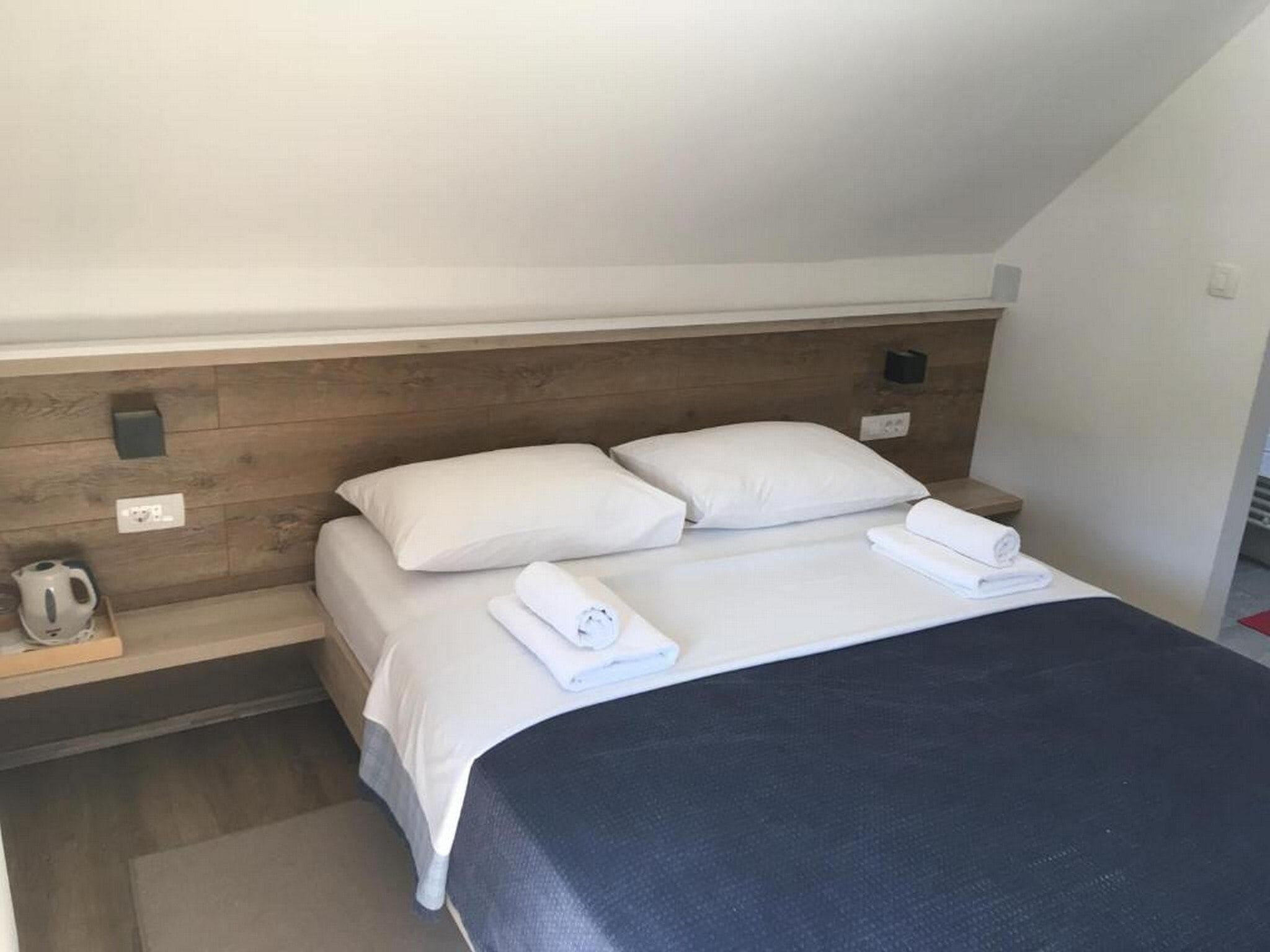 Ein Hotelzimmer mit Bett, zwei Kissen, einem Nachttisch mit Wasserkocher und einer Wandleuchte.