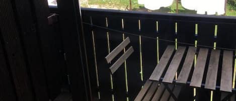 Un balcon donnant sur une zone boisée et un bâtiment situé au loin.