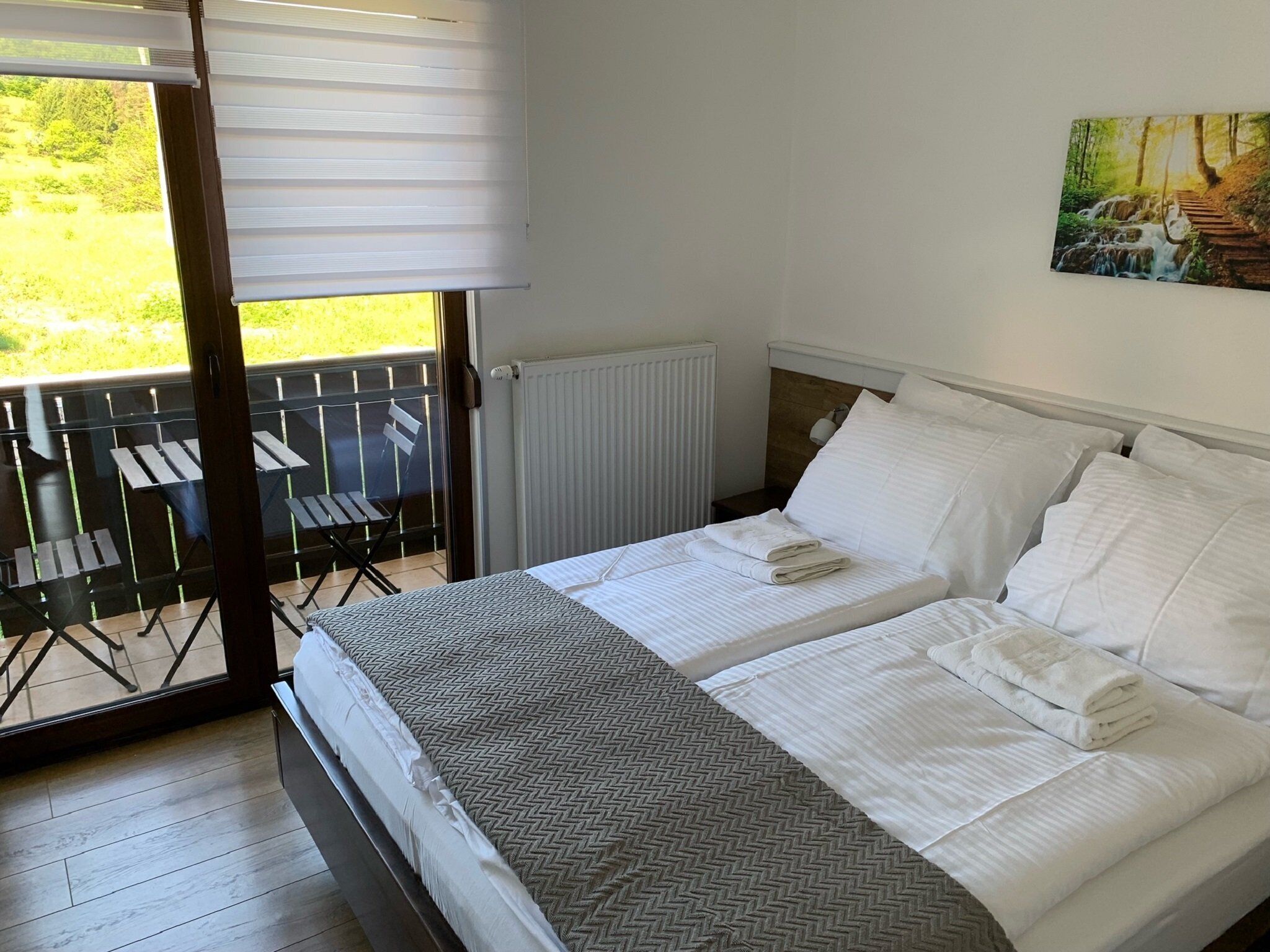Une chambre avec deux lits, un radiateur, un balcon avec des chaises et un tableau au mur.