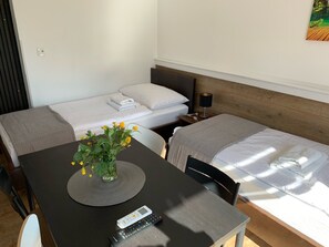 A hotel room with two single beds, a small table with a vase of flowers, a remote control, and a wall-mounted lamp.