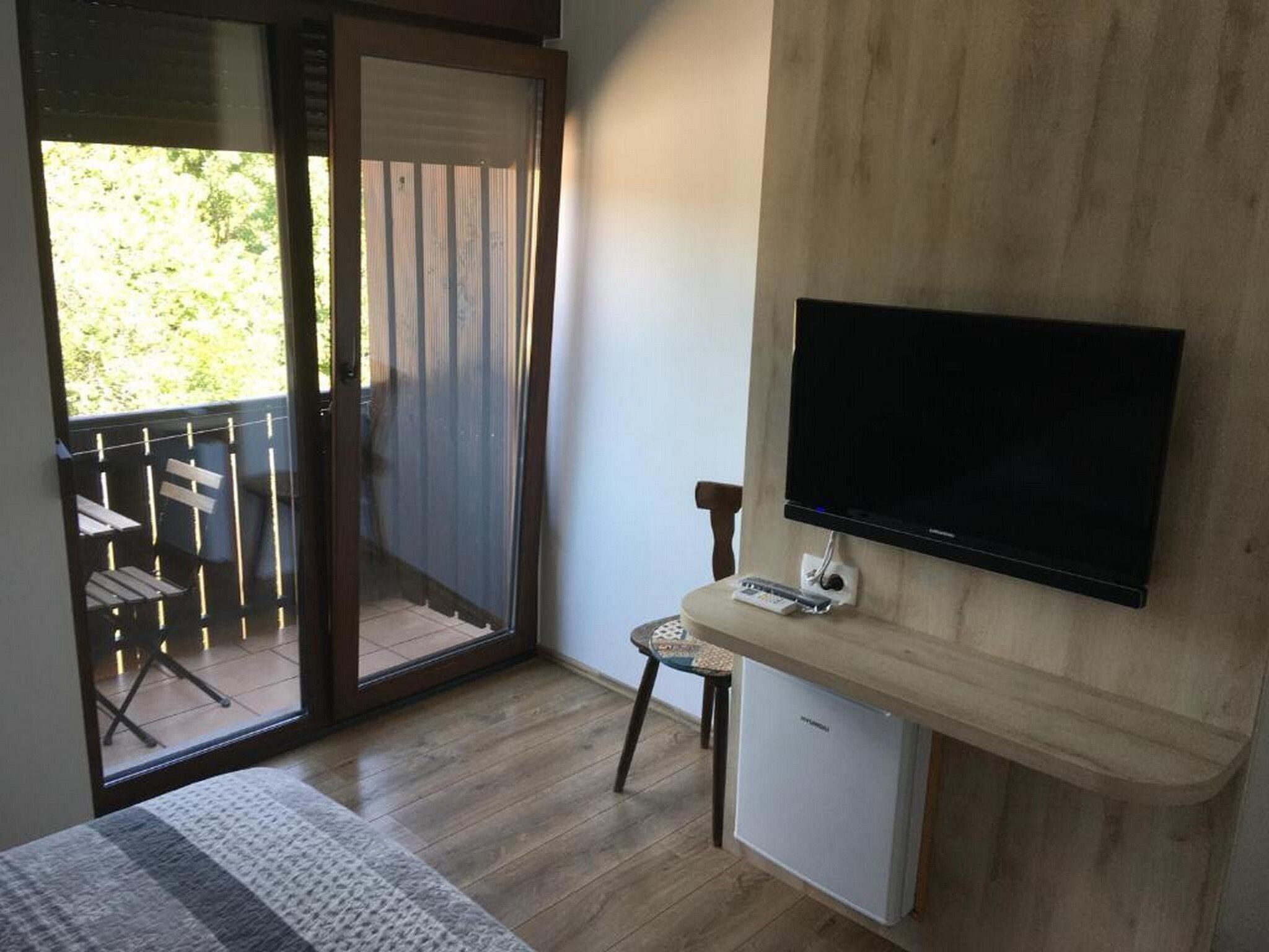 Una stanza con un letto, una TV a parete, un tavolino con una sedia e una porta finestra che dà su un'area esterna con tavolo e sedie.