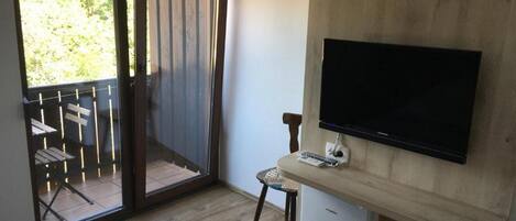 Una stanza con un letto, una TV a parete, un tavolino con una sedia e una porta finestra che dà su un'area esterna con tavolo e sedie.
