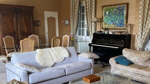 A living room with a sofa, armchairs, a coffee table, a piano, and a patterned rug.