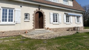A two-story house with a stone facade, a central wooden door, and multiple windows with shutters.