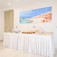 Zona de recepción de hotel con un mostrador blanco, un cuadro de una escena de playa y una ventana con cortinas color beige.
