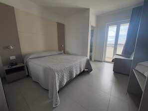 A modern hotel room with a large bed, a bedside table with a phone, a chair, and a view of the outdoors through a large window. - Hotel La Mela (Giugliano in Campania)