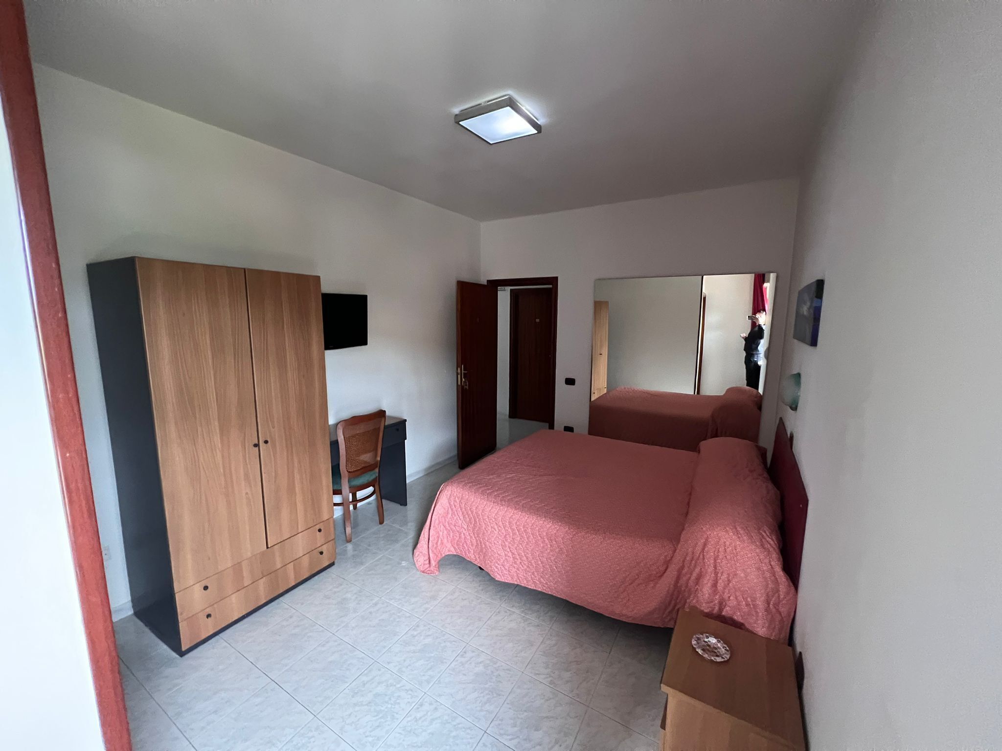 A bedroom with a bed, wardrobe, desk, chair, and a mirror.