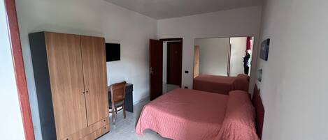A bedroom with a bed, wardrobe, desk, chair, and a mirror.