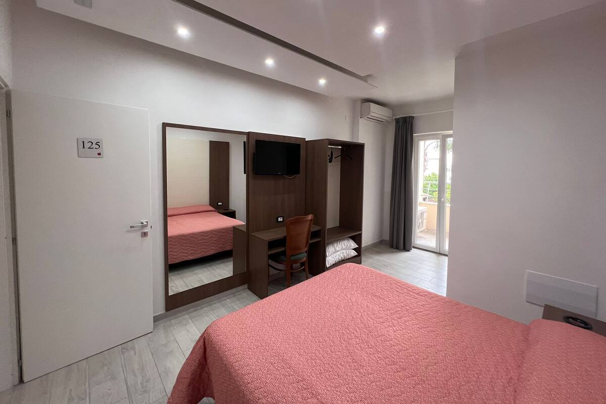 A bedroom with a bed, a wardrobe, a TV, and a sliding door leading to a balcony.