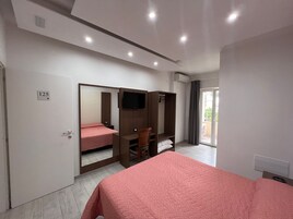 Un dormitorio con cama, armario, televisor y puerta corrediza que da a un balcón.