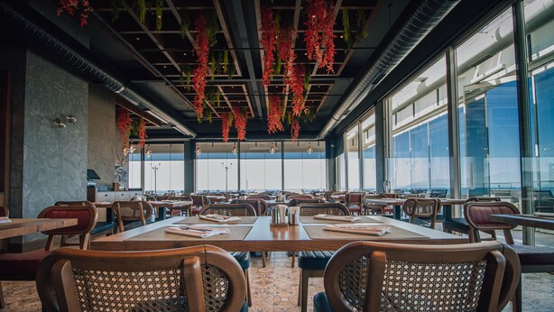 A spacious restaurant with high ceilings, hanging plants, and large windows offering a view. - Panagia Premier Trabzon (Trabzon)