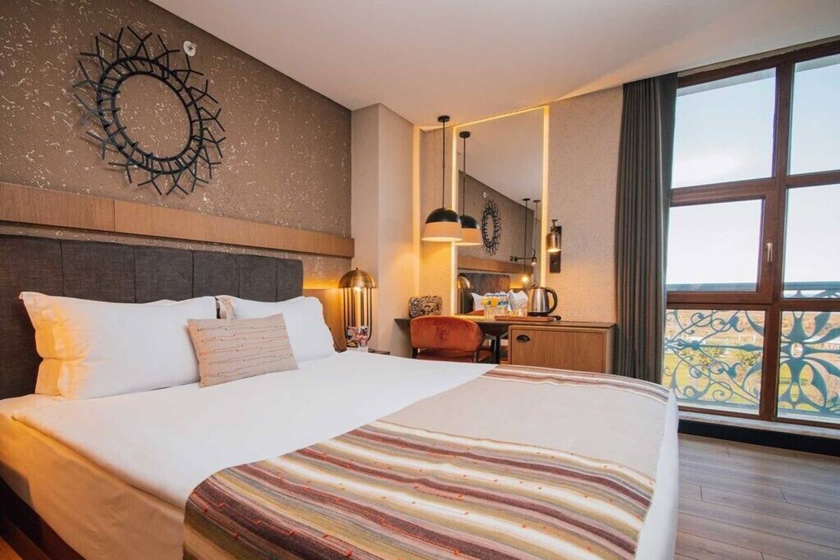 A hotel room with a large bed, a desk, a chair, and a view of the outdoors.