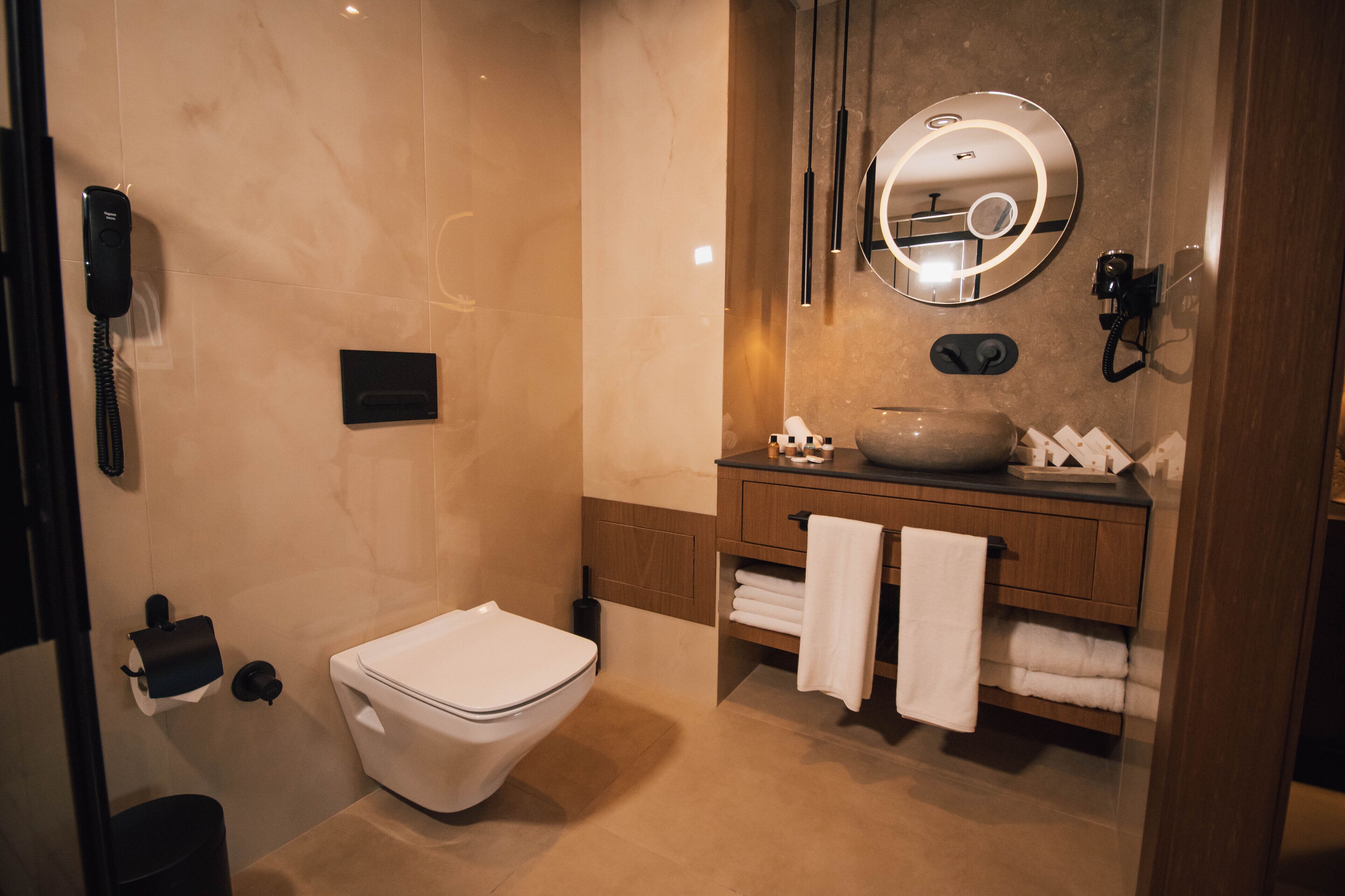 Een moderne badkamer met toilet, wastafel en spiegel met ringverlichting.