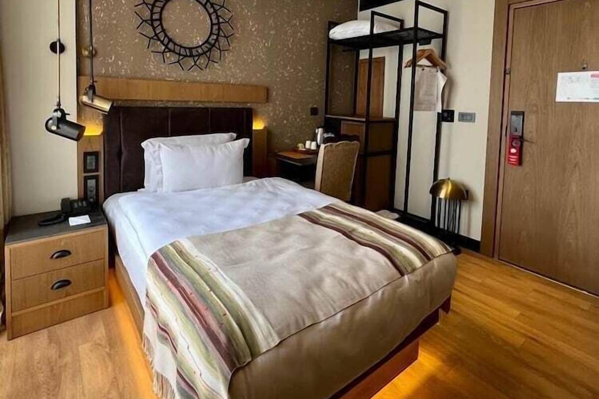 A hotel room with a bed, bedside tables, a mirror, a wardrobe, and a wall-mounted decorative piece.