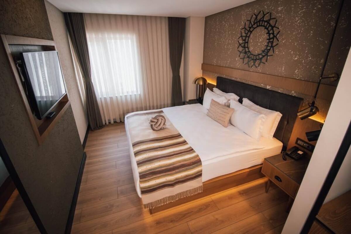 A hotel room with a large bed, a TV, a bedside table with a lamp, and a wall-mounted artwork.