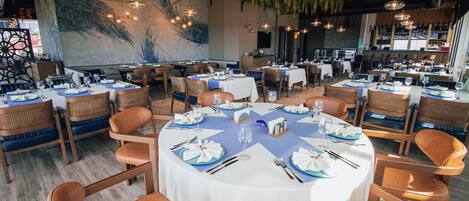 Un restaurante con mesas redondas dispuestas para comer, con manteles azules y servilletas blancas.