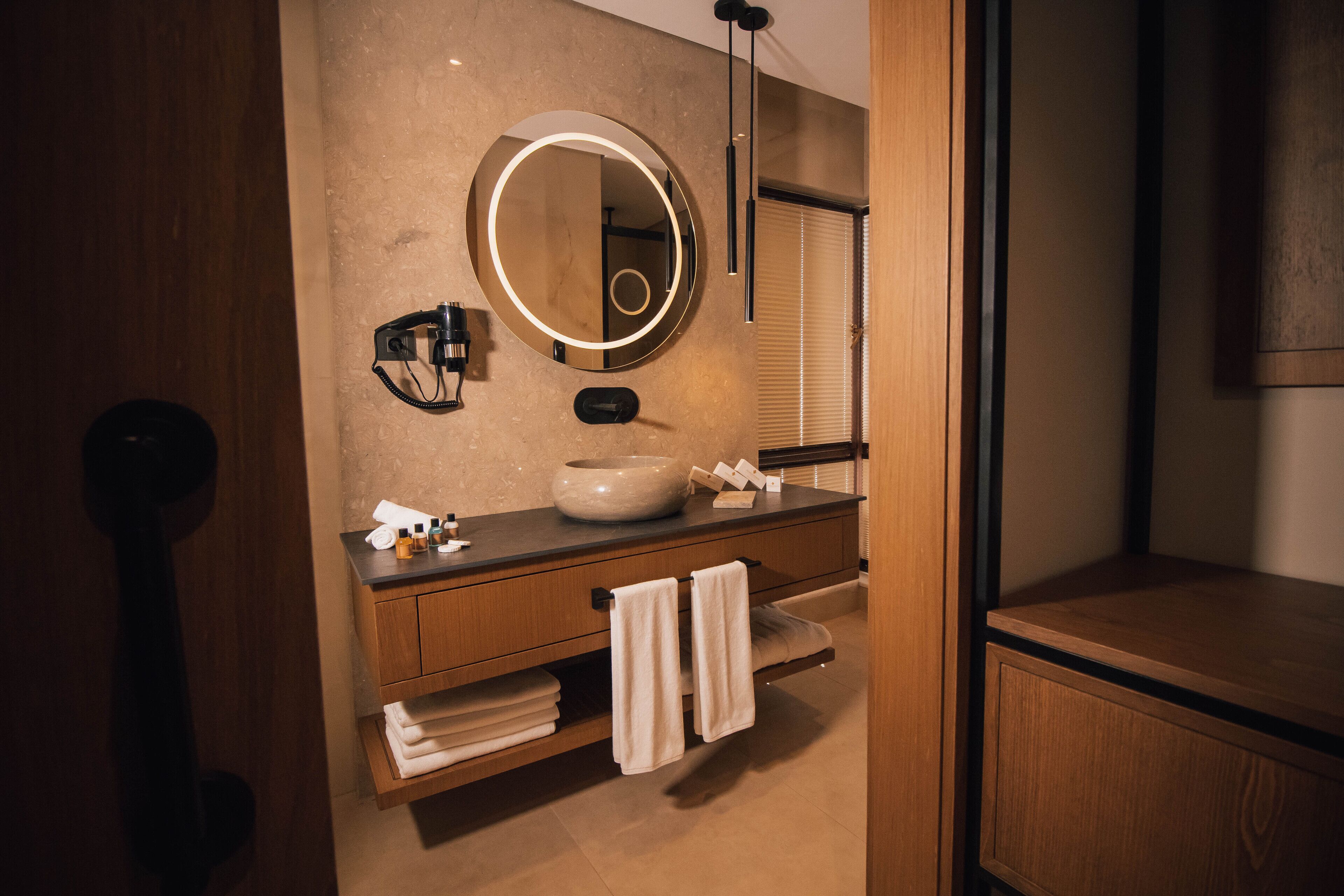 A modern bathroom with a round mirror, a sink, and wooden cabinetry.