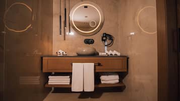 Un baño moderno con un espejo redondo, tocador de madera y toallas ordenadamente dobladas.