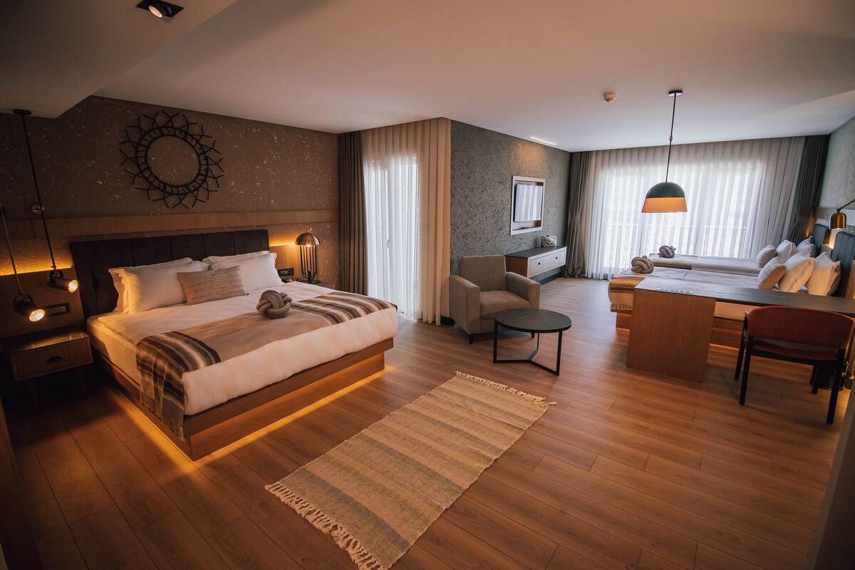 A modern hotel room with a large bed, a desk, and a comfortable seating area.