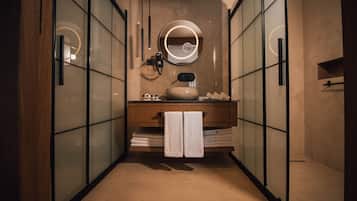 Une salle de bain moderne avec une cloison en verre, un meuble-lavabo en bois, un miroir rond et un porte-serviettes.