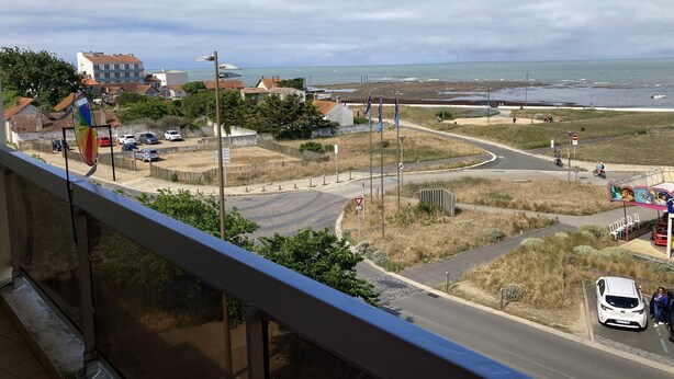 A coastal road with a view of the sea, a parking area, and a building with a red roof. - Apartment (Saint-Hilaire-de-Riez)