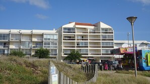 A multi-story hotel with balconies, a beachside location, and a colorful amusement ride nearby. - Apartment (Saint-Hilaire-de-Riez)