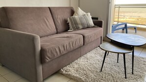 A living room with a brown sofa, a small round table, and a white shaggy rug. - Apartment (Saint-Hilaire-de-Riez)
