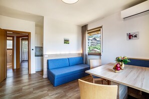 Une pièce moderne avec un plancher en bois, un canapé bleu, une table à manger avec des chaises, une fenêtre avec des rideaux et un petit coin cuisine.