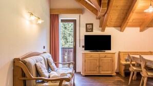 A cozy living room with a wooden sofa, a TV, a wooden dining table with chairs, and a wooden ceiling.