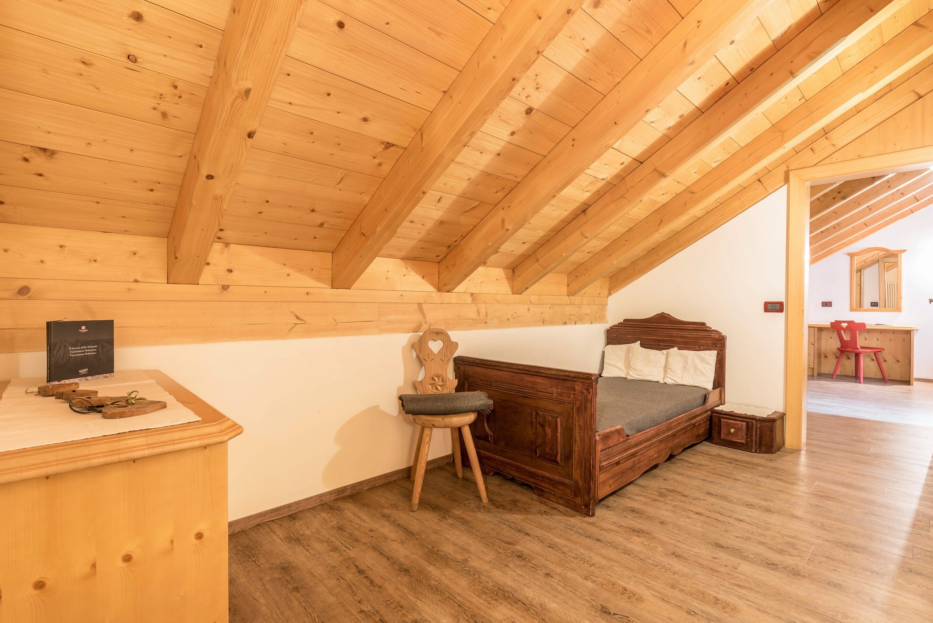 Eine Holzbalkendecke, ein Bett, ein Stuhl, ein Schreibtisch und ein kleiner Tisch in einem Zimmer.