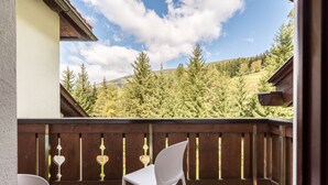 A balcony with a white chair, a wooden fence, and a view of a forested hillside.