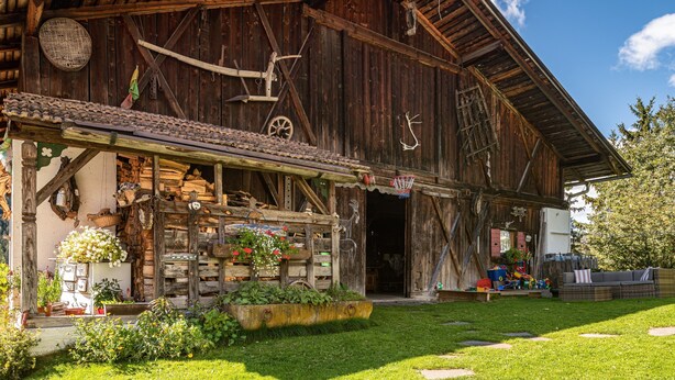 A rustic wooden barn with a covered porch, a basketball hoop, and a garden area with flowers and plants.